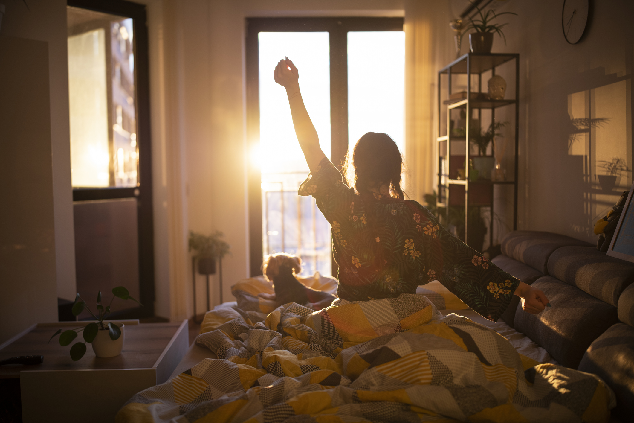 The Best Direction to Sleep In Young woman streching in bed in the morning while looking at the sunrise.