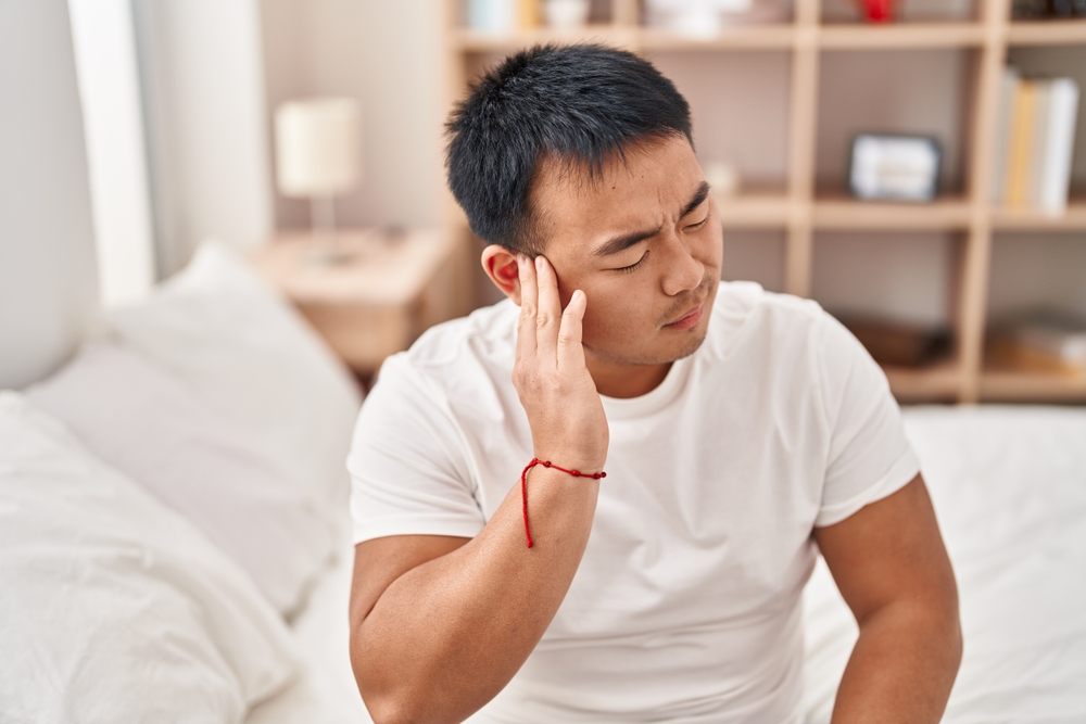 What Side Should You Sleep on if You Have a Ruptured Eardrum? A young man holding his ear with a pained expression