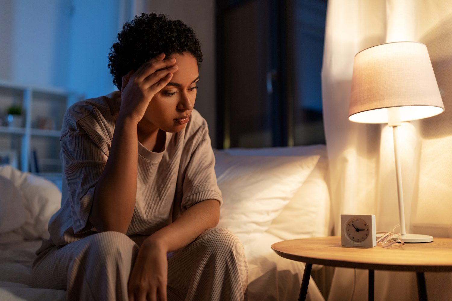 Interrupted Sleep: Causes & Helpful Tips A woman sits on the edge of a bed unable to sleep