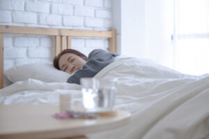 Woman sick in bed with a bottle of pills and a glass of water ont he table