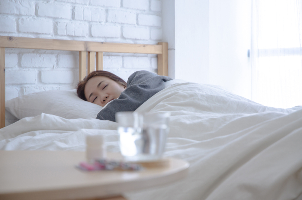 Woman sick in bed with a bottle of pills and a glass of water ont he table