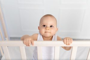 8-Month Sleep Regression portrait of a smiling baby boy 8 months old standing in a crib